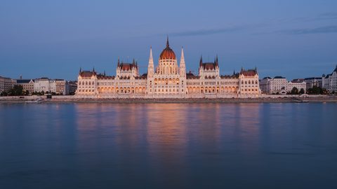 The illuminated Hungarian Parliament building reflected in the Danube River at dusk.