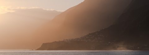 Warm hazy light falling across a steep coastline and a small clifftop village.