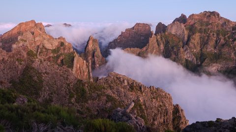 Jagged volcanic peaks rising above a sea of clouds at sunrise.